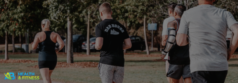 A group of five people jogging on a gravel path in a park surrounded by trees and greenery.