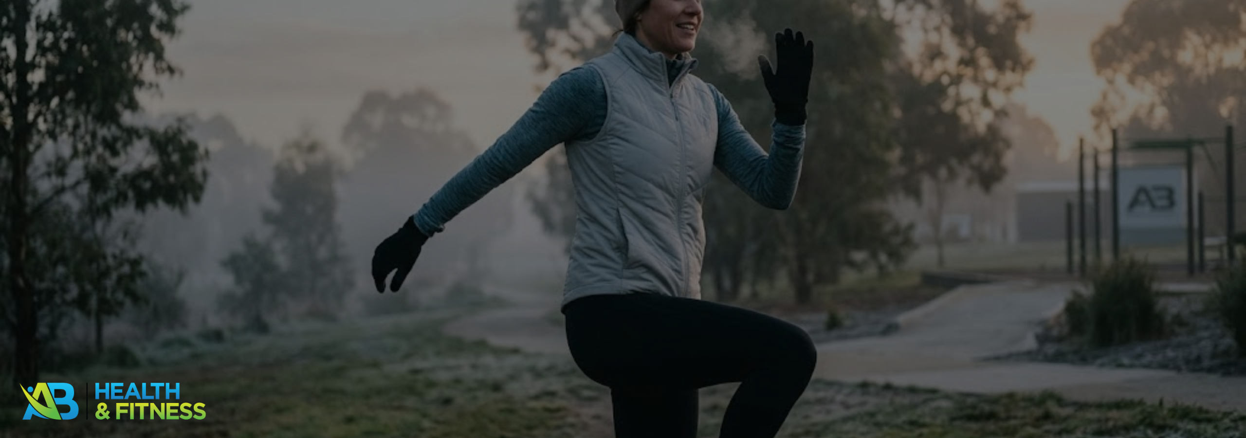 A woman warming up dynamically in a misty Melbourne park on a cold morning, wearing winter activewear with her breath visible.